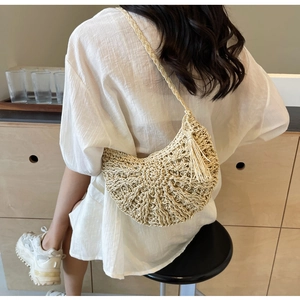 Detail of hand-woven straw crossbody bag with decorative tassel and braided strap