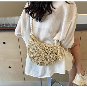Detail of woven straw shoulder bag with side tassels and radial pattern on textured surface