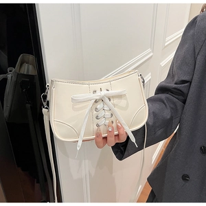 Detail einer cremeweißen Schultertasche mit Schnürschleifen-Design und silbernen Metallösen