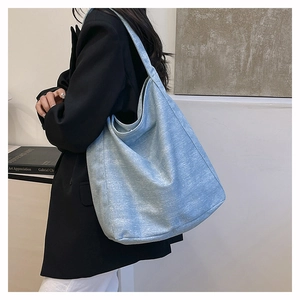 Detail of glittery light blue canvas tote bag worn by model in black suit for daily wear