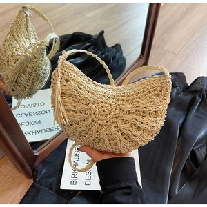 Mirror reflection showing details of beige woven straw crescent bag with tassel