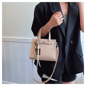 Minimalist beige pebble leather handbag with metal turn-lock and woven charm decoration