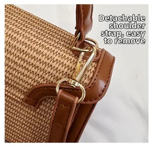 Detail of straw handbag featuring gold metal hook and detachable brown leather strap