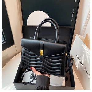 Detail of black wave quilted handbag with gold clasp in premium gift packaging