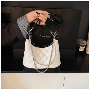 Detail of white quilted handbag with black contrast trim and silver metal chain strap