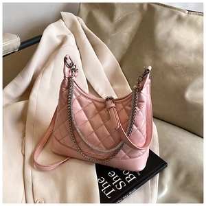 Detailed close-up of pink quilted crossbody bag with metal chain strap on blazer