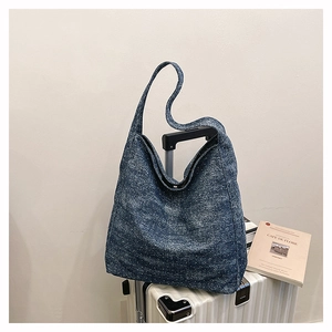 Detail of blue denim hobo bag hanging on white luggage showing vintage canvas texture