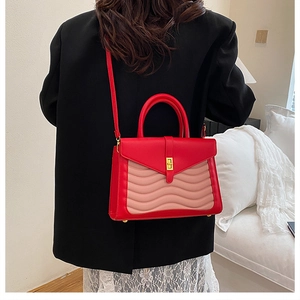 Detail of pink wavy quilted texture and golden twist lock on a red crossbody bag