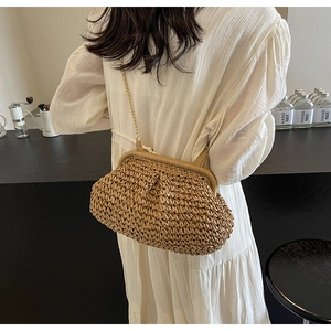 Détail d'un sac bandoulière en paille tressée avec chaîne dorée sur robe blanche