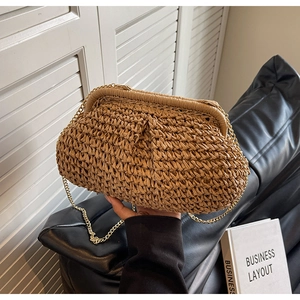 Détail d'une pochette en paille tissée avec chaîne dorée et texture plissée naturelle