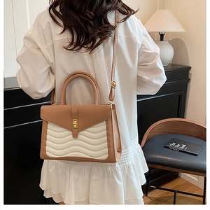 Brown and white crossbody bag with gold turn-lock shown in a modern home setting