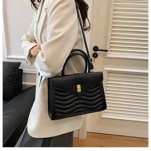 Detail of black wave quilted pattern leather bag with golden turn-lock closure and handles