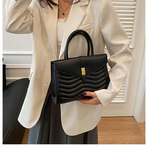 Detail of black wave quilted handbag with a gold rectangular metal buckle and sturdy handles