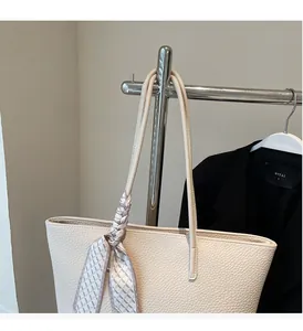Close-up of beige tote bag with lychee texture and decorative silk scarf on handle