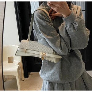 Close-up of cream leather shoulder bag featuring woven flap design and gold lock detail