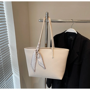 Close-up of cream tote bag with pebble texture and decorative silk scarf on handle