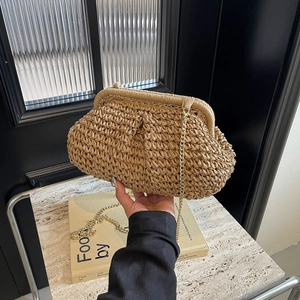 Sac nuage en paille tressée beige avec bandoulière chaîne dorée porté élégamment à la main