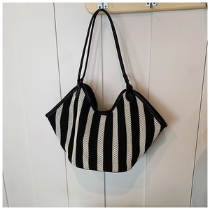 Detail of black and white striped woven tote bag with leather straps on a white wood wall