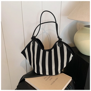 Close-up of black and white striped woven tote bag with premium leather handles on books