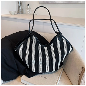 Striped woven tote bag with slim black straps displayed on a cozy minimalist sofa