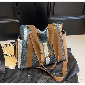Detail of striped canvas tote bag with brown woven handles and adjustable shoulder strap