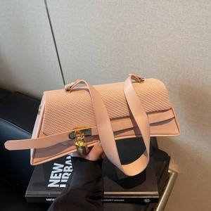 Pink geometric crossbody bag with textured woven flap and gold buckle on a book