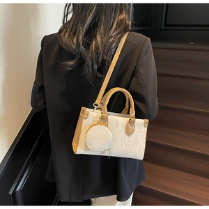 Detail of crossbody bag with pleated texture and round pendant on dark suit background