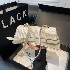 Chic cream-colored shoulder bag with woven flap and gold padlock held against gift bags