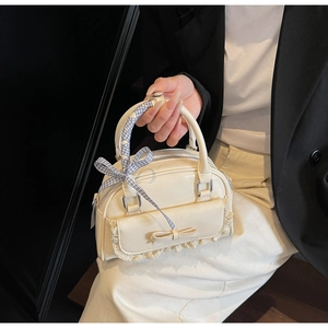 Chic cream bow handbag with lace trim and ribbon handle held against dark blazer