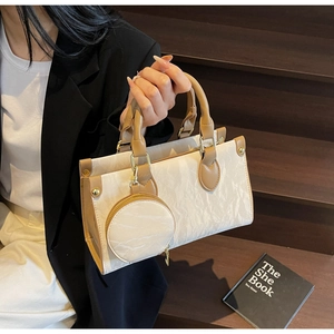 Detail of cream pleated crossbody bag with brown handles and a round coin purse charm