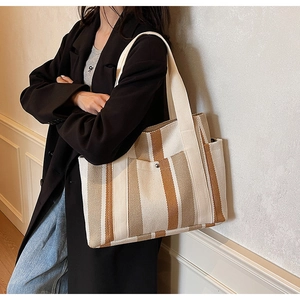 Detail view of large striped canvas tote bag showing side pocket and woven shoulder strap