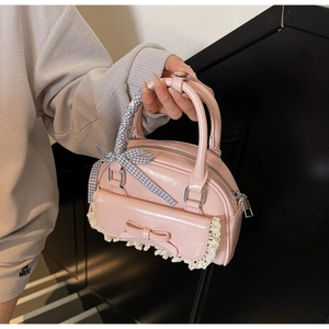 Detail of pink glossy patent leather handbag featuring bow, lace, and plaid ribbon