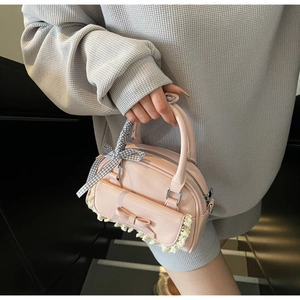 Pink crossbody bag with a bow, lace detail, and ribbon wrapped handle held by a model