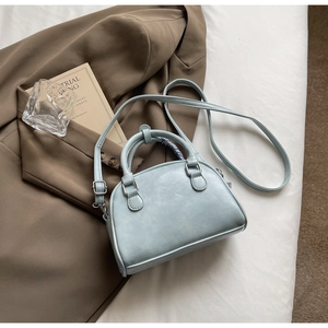 Detail of light blue PU leather handbag with silver metal buckles on a white cloth background