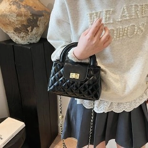 Detail of black quilted crossbody bag with golden twist-lock and chain strap on art deco shelf