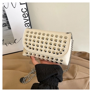 Detail of a beige quilted crossbody bag with silver studs and a metallic chain strap