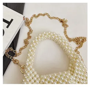 Close-up of handmade white pearl woven handbag featuring a thin gold chain strap