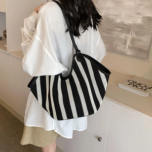 Large black and white striped woven tote bag with leather straps on model's shoulder