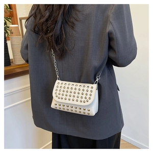 Chic white leather crossbody bag with silver studs and chain strap in a cafe setting