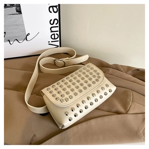 Close-up of cream white studded shoulder bag with silver rivets on a trench coat background