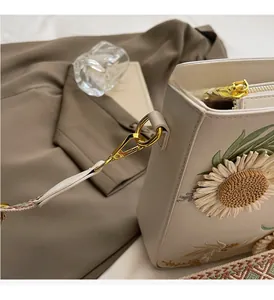 Detailed shot of beige shoulder bag featuring floral embroidery and golden metal hardware
