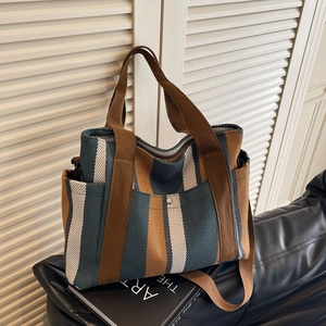 Large striped canvas tote bag with brown handles and crossbody strap on a sofa