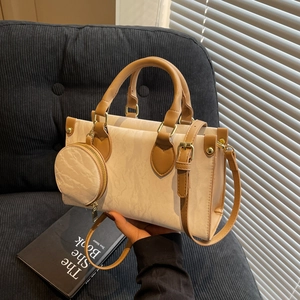 Chic cream shoulder bag with brown handles and a round coin purse on a black sofa