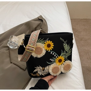 Close-up of sunflower embroidery on black crossbody bag with wide woven strap