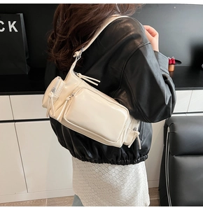 Detail of a shiny cream faux leather crossbody bag with multiple zip pockets and compartments