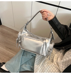 Detail of silver metallic shoulder bag showing multiple zipper pockets and sleek textures