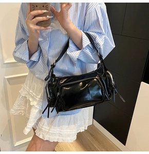 Close-up of black glossy patent leather Y2K shoulder bag with multiple functional zippers