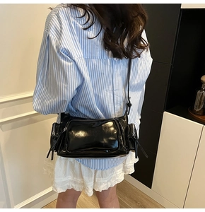 Model wearing a vintage black patent leather moto bag with multiple zip pockets