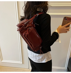 Detail view of burgundy patent leather bag with multiple zippers and adjustable strap