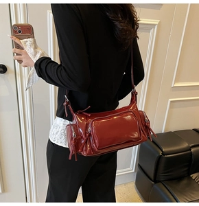 Detail of burgundy glossy crossbody bag featuring multiple zippers and vintage biker style